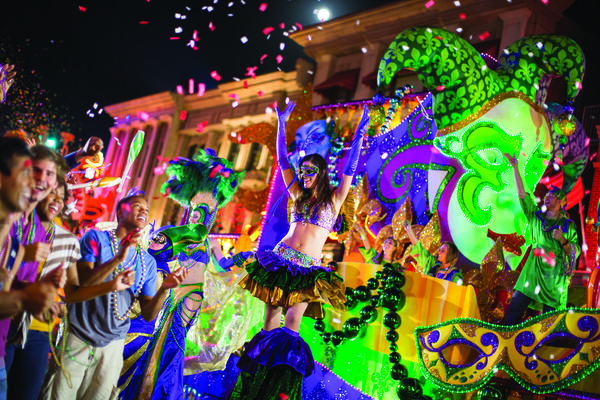 Group of people standing in front of a Universal Mardi Gras parade as entertainers cheer them on