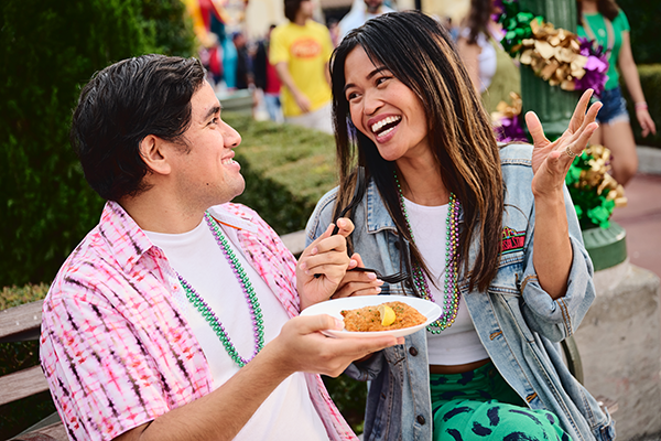 Couple sitting at a bench during Universal Mardi Gras enjoying food